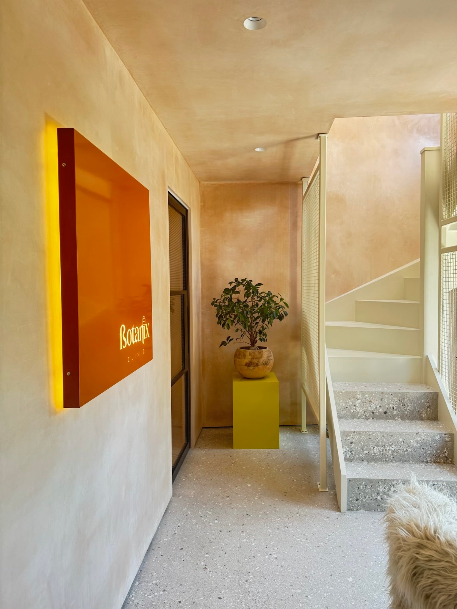 Botanix Clinic,interior design by house of Bo, raw plaster walls, microcement floor and stairs, pocket door, powder coated contemporary staircase, laser-cut metal signage, recessed spotlights. Kaia Plinth Block Side Table by Anthropologie.